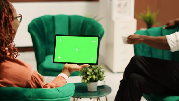 Tourists in hotel lobby being assisted by manager, holding chroma key green screen mock up tablet in landscape mode. Resort administrator helping guests during check in process