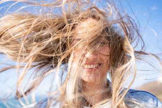 Closeup of young woman face covered with flying hair in windy day. Portrait female with hair blowing in the wind. Wanderlust autumn travel, atmospheric moment