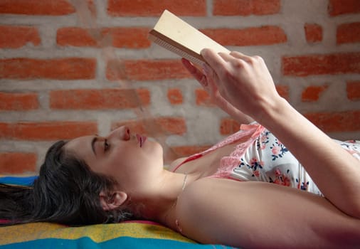 attractive young woman from ecuador lying on her back on her bed in her nightclothes reading a book attentively in the morning after waking up. book day. High quality photo