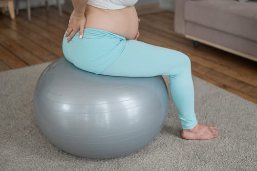 Caucasian pregnant woman suffers from back pain. Fitball training during pregnancy