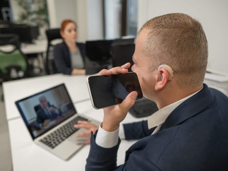 Caucasian man with a hearing aid talking on the phone on speakerphone