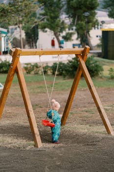 Little girl holds the swing seat behind her to sit on. Back view. High quality photo