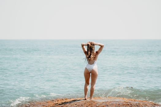 Woman sea yoga. Back view of free calm happy satisfied woman with long hair standing on top rock with yoga position against of sky by the sea. Healthy lifestyle outdoors in nature, fitness concept.