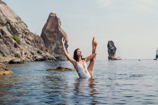 Young woman with black hair, fitness instructor in pink sports leggings and tops, doing pilates on yoga mat with magic pilates ring by the sea on the beach. Female fitness daily yoga concept