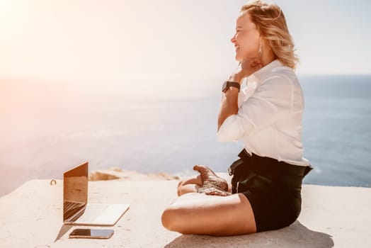 Happy girl doing yoga with laptop working at the beach. beautiful and calm business woman sitting with a laptop in a summer cafe in the lotus position meditating and relaxing. freelance girl remote work beach paradise