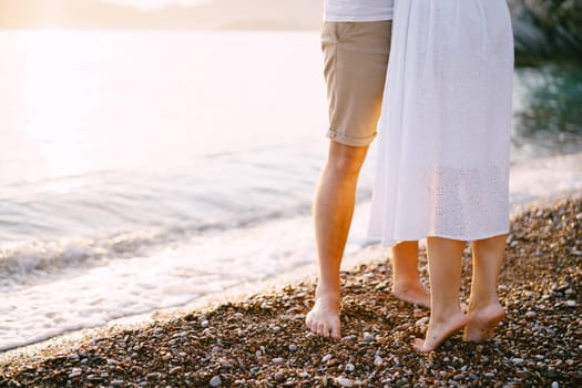 Woman is standing on tiptoe next to man on a pebbly beach. Cropped. Faceless. High quality photo