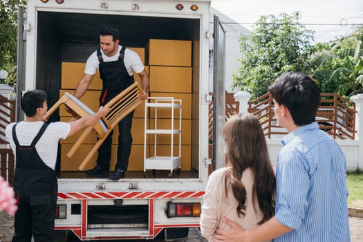 Newlywed couple receives seamless moving service to their new house. A dedicated team unloads and lifts cardboard boxes showcasing efficient delivery logistics. Moving Day Concept