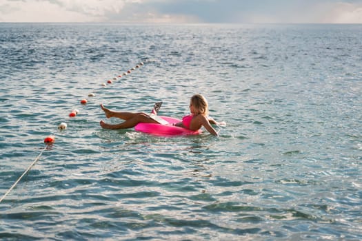 Woman works on laptop in sea. Freelancer, blond woman in sunglases floating on an inflatable big pink donut with a laptop in the sea at sunset. People summer vacation rest lifestyle concept