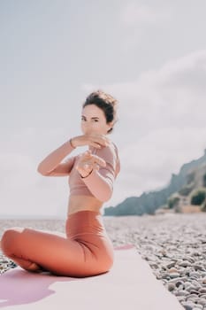 Young woman with long hair in white swimsuit and boho style braclets practicing outdoors on yoga mat by the sea on a sunset. Women's yoga fitness routine. Healthy lifestyle, harmony and meditation