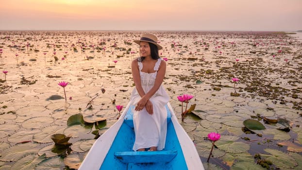 The sea of red lotus, Lake Nong Harn, Udon Thani, Thailand. Asian woman with a hat and dress on a boat at the Red Lotus Lake in the Isaan