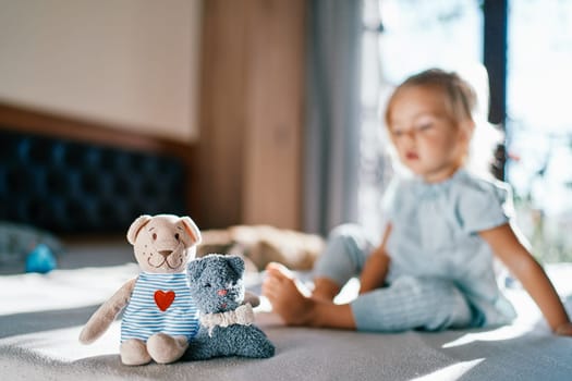 Teddy bear and a toy cat are sitting on the bed embracing against the background of a little girl. High quality photo