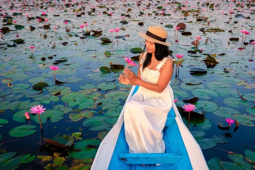 The sea of red lotus, Lake Nong Harn, Udon Thani, Thailand. Asian woman with hat and dress on a boat at the red lotus lake in the Isaan