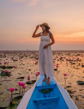 Sunrise at the sea of red lotus, Lake Nong Harn, Udon Thani, Thailand. Asian woman with a hat and dress on a boat at the Red Lotus Lake in the Isaan