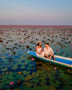 The sea of red lotus, Lake Nong Harn, Udon Thani, Thailand, a couple of men and woman in a boat at sunrise at the Red Lotus Lake in the Isaan, drone aerial view