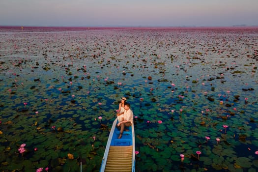 Drone aerial view at the sea of red lotus, Lake Nong Harn, Udon Thani, Thailand, a couple of men and woman in a boat at sunrise at the Red Lotus Lake in the Isaan