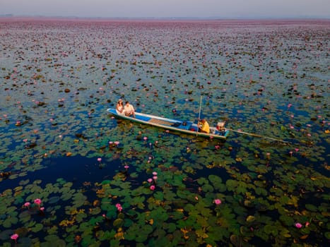 The sea of red lotus, Lake Nong Harn, Udon Thani, Thailand, a couple of men and woman in a boat at sunrise at the Red Lotus Lake in the Isaan