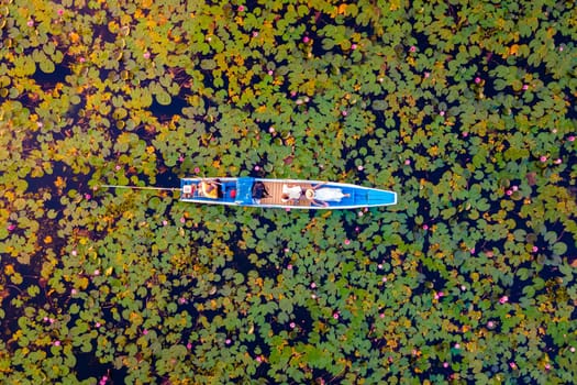 The sea of red lotus, Lake Nong Harn, Udon Thani, Thailand, a couple of men and woman in a boat at sunrise at the Red Lotus Lake in the Isaan