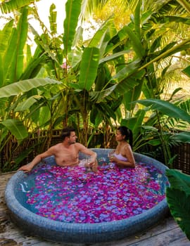 a couple of man and women in an outdoor bathtub in a green garden with leaves, couple of men and woman in a bath tub with flowers at sunset in an outdoor bathroom