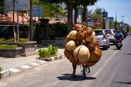 A motorcycle heavily loaded with wicker baskets is driving through the streets of an Indonesian village. Bali, Indonesia - 12.08.2022