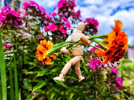 Wooden toy man with flowers against background grass in nature. Concept of holiday, gift bouquet, Valentine's Day, proposal, engagement, declaration of love, Mother's Day. Caring, loving and romantic