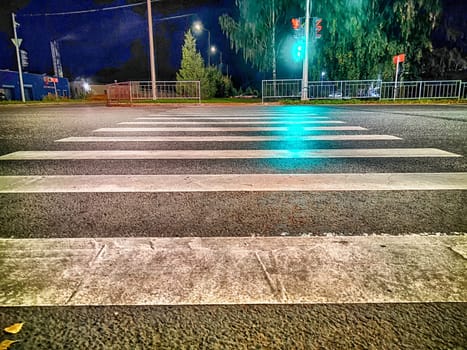 View of the pedestrian crossing strips and the burning traffic light on the other side of the road and street in the dark at night