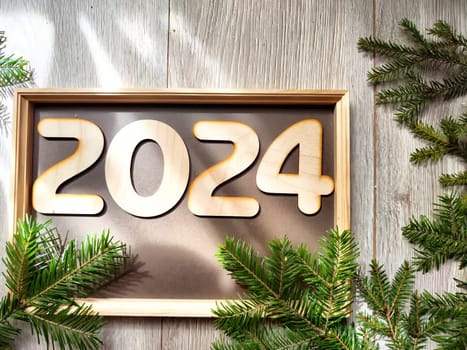 Wooden figures and numbers of the new year 2024 with frame and fir branches of Christmas tree. Celebration. Abstract background, pattern, frame, place for text, copy space
