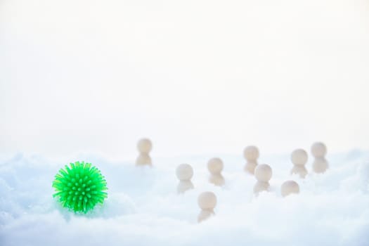 Green ball with appendages similar to the coronavirus, wooden men around and snow. COVID-19 disease is more common in winter in the cold