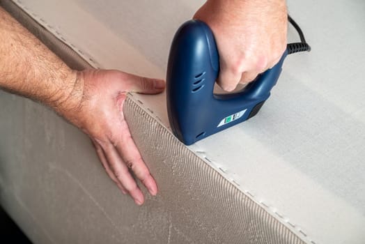 Worker stapling sofa lining with electric staple gun