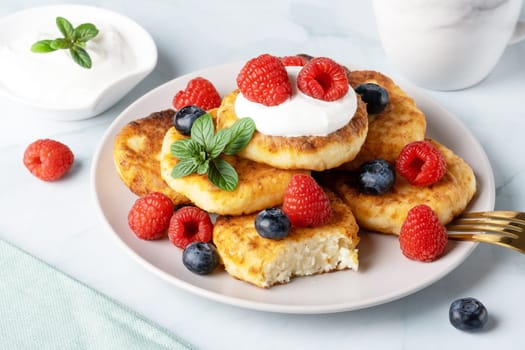 Cottage cheese pancakes with raspberries and blueberry on light background, breakfast or lunch.