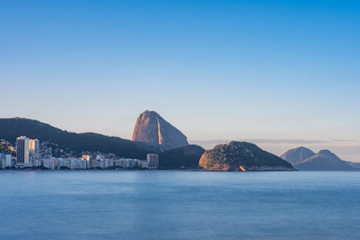 Long exposure photo of Copacabana beach, featuring Sugarloaf Mountain, calm water, and dusk sky.