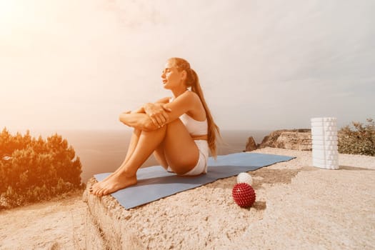 Middle aged well looking woman with black hair doing Pilates with the ring on the yoga mat near the sea on the pebble beach. Female fitness yoga concept. Healthy lifestyle, harmony and meditation.