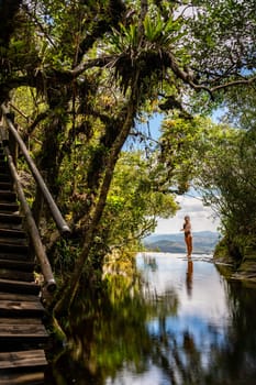 Woman in serene forest pool surrounded by verdant foliage, her reflection on calm water.