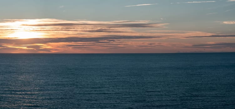 Peaceful ocean with vivid sunset and reflective clouds.