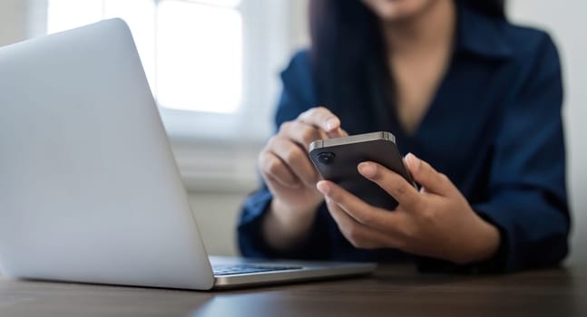 Young business woman on the phone at office. Business woman texting on the phone and working on laptop. Pretty young business woman sitting on workplace.