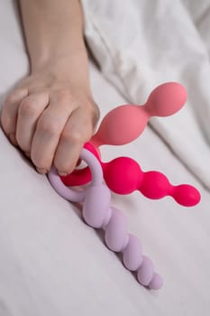 Woman holding three different anal beads while lying in bed