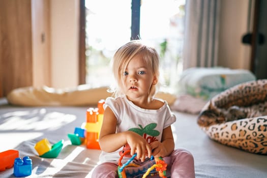 Little girl collects puzzle rattle sitting on the bed. High quality photo