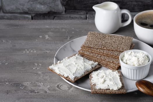 Crispy rye crackers with cottage cheese on a gray wooden table.