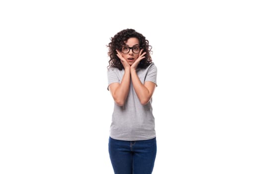 smart young curly brunette woman with glasses for vision in a gray t-shirt on a white background with copy space.