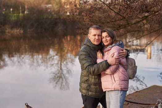 Loving couple sit on the shore of the pond in the park in autumn. A man and a woman. A couple, lovers on the shore of the lake on a walk