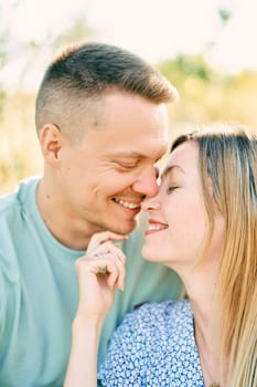 Smiling husband touches wife nose with his nose while sitting hugging in field. High quality photo