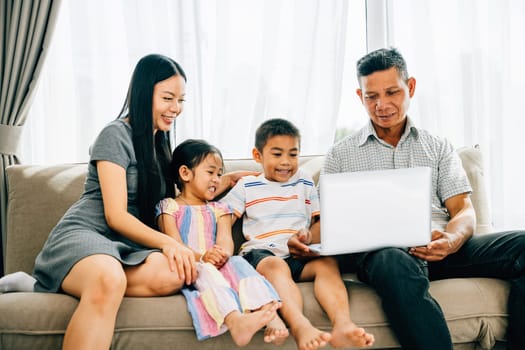 Parents and children happily share a laptop on a sofa browsing contentedly. This image portrays familial bonding joy and the wonder of shared technology experiences within the family.