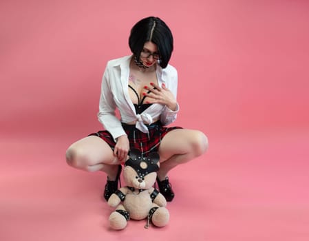 BDSM teddy bear in the hands of a sexy woman in a schoolgirl costume for sexual role-playing games on a pink background, copy paste, a banner for a sex shop
