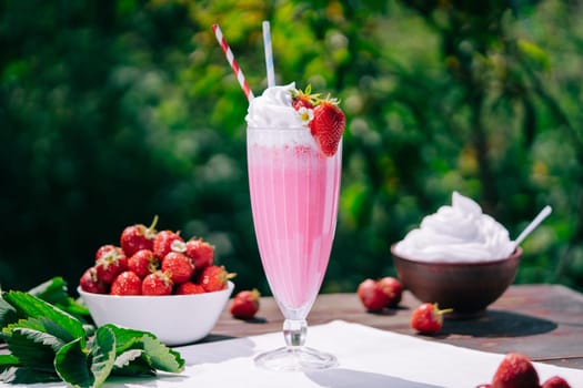 Still life - creamy strawberry milkshake cocktail or smoothie with straw on nature backdrop. Appetizing summer dessert. Healthy berry food. High quality