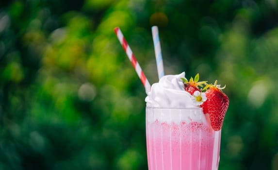 Still life - creamy strawberry milkshake cocktail or smoothie with straw on nature backdrop. Appetizing summer dessert. Healthy berry food. High quality