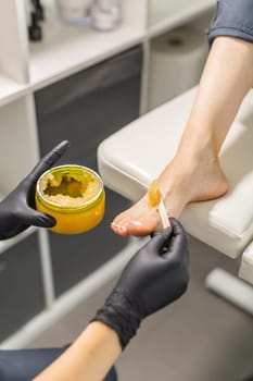 Woman doing foot peeling in pedicure SPA salon. Sugar scrub and relax beauty procedure.