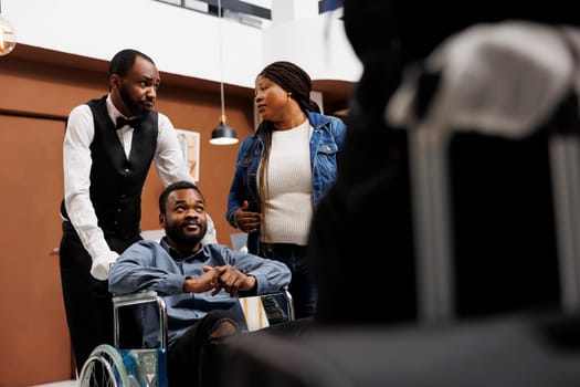 Hotel bellman transferring disabled guest on wheelchair to room, happy young African American handicapped man enjoying customer service for people with disabilities, accessible tourism