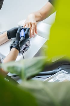 Manicurist uses an electric drill to remove old gel polish from nails. A woman is getting a manicure of nails. The beautician files the client's nails. professional manicure tool. Close-up.