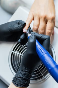 Nail manicure in woman beauty salon. Electric nails file drill in action, finger close up or detail with color background