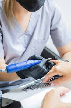 Nail manicure in woman beauty salon. Electric nails file drill in action, finger close up or detail with color background