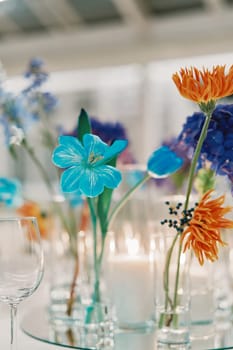 Bright colorful flowers stand in glasses on a set table. High quality photo